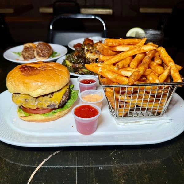 A cheeseburger with lettuce and tomato, a basket of fries, and three dipping sauces on a white plate.