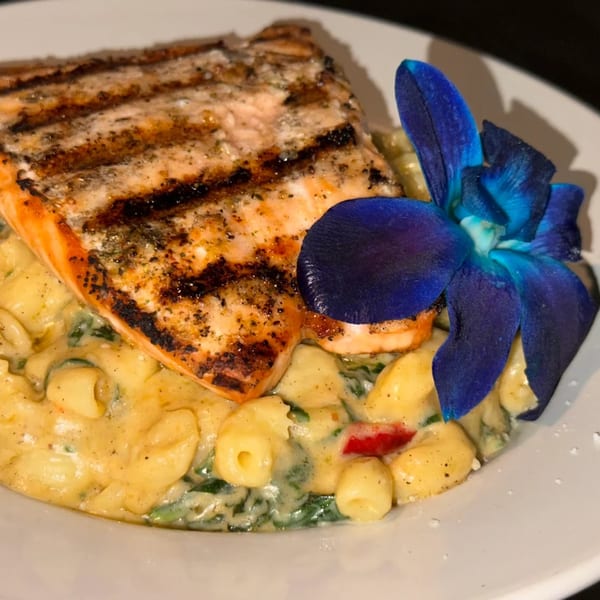 Grilled salmon with grill marks, served over creamy pasta with spinach and a blue orchid garnish.