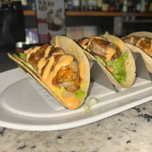 Three shrimp tacos with lettuce and a creamy orange sauce on a white plate at Silk Restaurant.