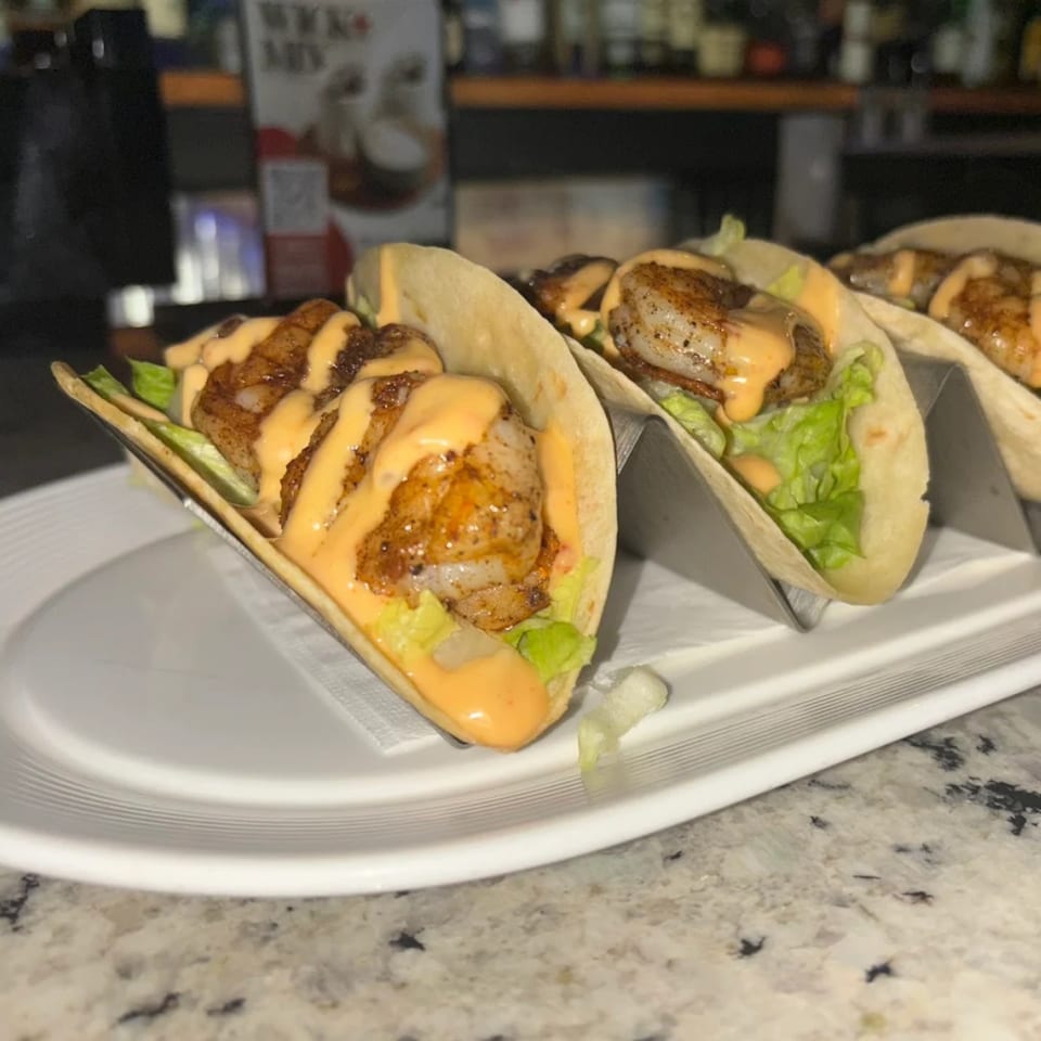 Three shrimp tacos with lettuce and a creamy orange sauce on a white plate at Silk Restaurant.