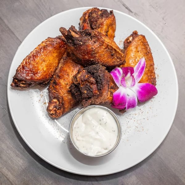 Crispy American-style chicken wings with a side of ranch dressing, garnished with a purple orchid.