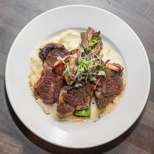 Grilled lamb chops on a bed of mashed potatoes, garnished with microgreens, served on a white plate.