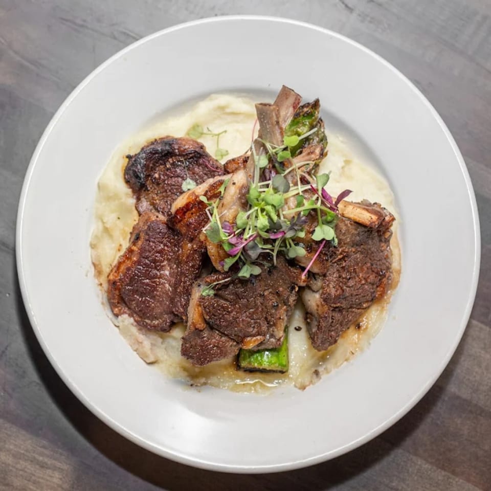 Grilled lamb chops on a bed of mashed potatoes, garnished with microgreens, served on a white plate.