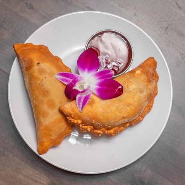 Two golden-brown American empanadas with a side of dipping sauce and a purple orchid on a white plate.